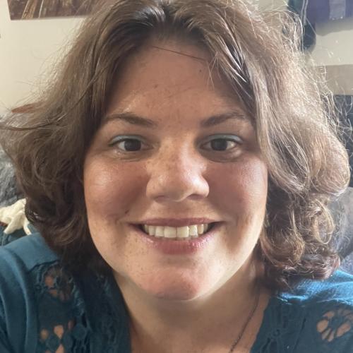 Megan Shrader Image Description: Megan has short, wavy brown hair, dark eyes, and a round face. She wears a jewel-toned blue blouse.